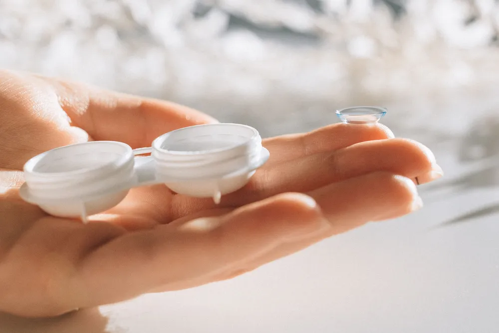 A contact lens resting on a fingertip beside an open lens case